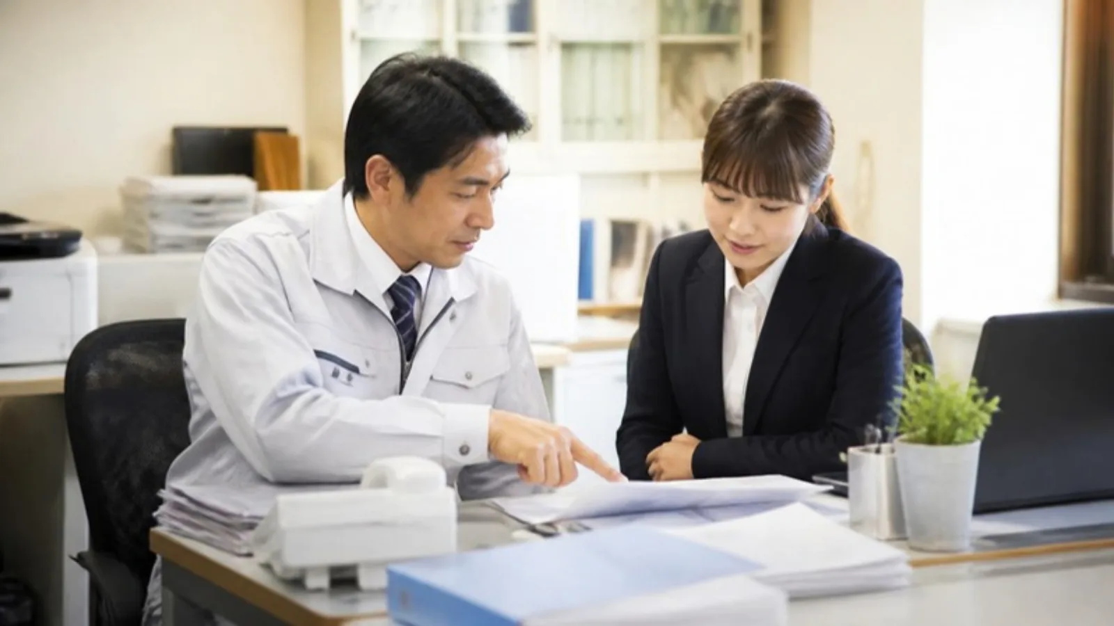 小さな事務所で書類を挟んで打ち合わせをする二人